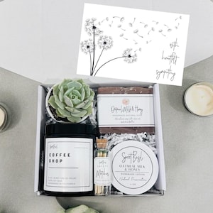 Puede incluir: Una caja de regalo llena de art&iacute;culos para el cuidado personal, que incluyen una peque&ntilde;a planta suculenta, una vela, una pastilla de jab&oacute;n, un peque&ntilde;o frasco de loci&oacute;n y una caja de cerillas. La caja est&aacute; decorada con papel de seda blanco y una tarjeta con un dise&ntilde;o de diente de le&oacute;n y las palabras "con sentidas condolencias".