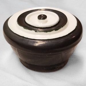 May include: A black and white ceramic bowl with a lid. The lid has a concentric circle design with a green accent. The bowl has a textured surface.