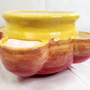May include: A yellow and red ceramic planter with four individual planting sections. The planter has a rounded shape and a smooth, glossy finish.