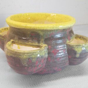 May include: A yellow and brown ceramic planter with four individual planting sections. The planter has a speckled glaze and a rounded shape.