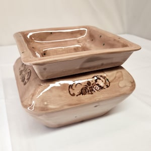 May include: A light brown ceramic planter with a square top and a decorative design on the bottom. The planter has a removable top that can be used as a separate dish.