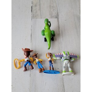 May include: A collection of Toy Story character figurines, including Woody, Buzz Lightyear, and Rex the dinosaur. The figures are brightly colored and made of plastic, with detailed features. The characters are posed in various action stances.