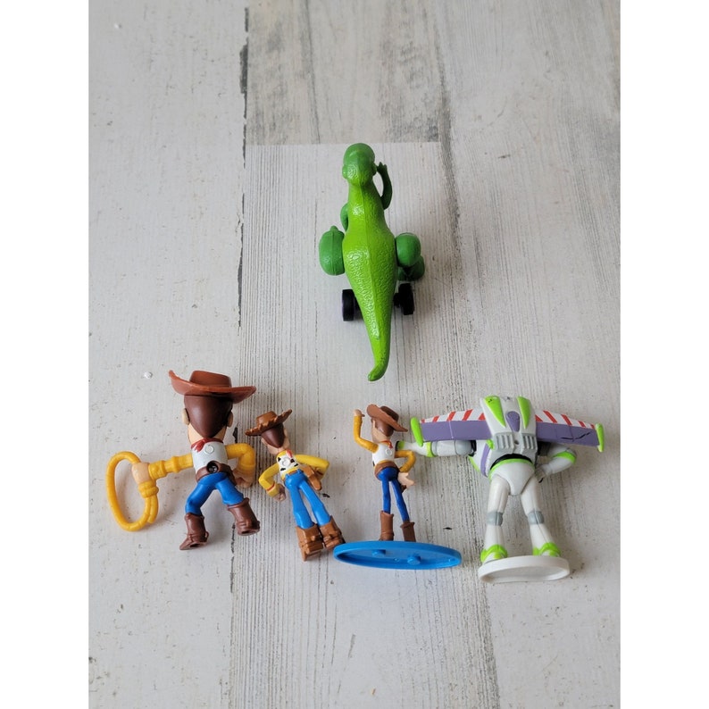May include: A collection of Toy Story character figurines, including Woody, Buzz Lightyear, and Rex the dinosaur. The figures are brightly colored and made of plastic, with detailed features. The characters are posed in various action stances.