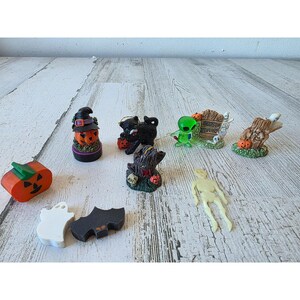 Può includere: Una collezione di figurine in miniatura a tema Halloween. Include una zucca arancione, un fantasma, un pipistrello, una zucca con cappello da strega, un gatto nero, un ceppo d'albero, un alieno e uno scheletro.