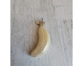 May include: A gold-coloured glass bauble shaped like a crescent moon. The bauble has a textured surface and a silver loop for hanging.
