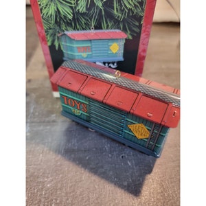 May include: A red and green toy train carriage ornament with the word "TOYS" and the number "97" on the side. The carriage is labelled "Yuletide Central" and has a gold loop for hanging.
