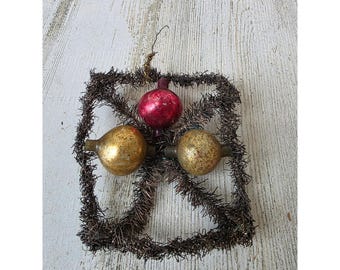Puede incluir: Adorno navideño vintage con un marco cuadrado de oropel marrón, que sostiene tres bombillas de cristal. Las bombillas son doradas y rojas, con un aspecto texturizado y envejecido. Hay un pequeño lazo en la parte superior para colgar.