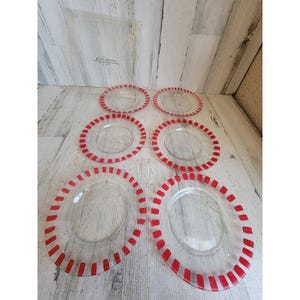 May include: A set of six clear glass plates arranged in three rows of two. Each plate features a distinct red striped pattern along the outer rim. The plates are displayed in their original transparent packaging with the text glass plates visible.