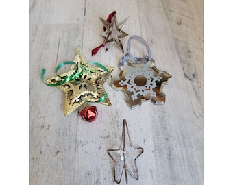 May include: A selection of Christmas decorations, featuring star and snowflake designs. The ornaments are in gold, silver, and clear, with red and green ribbons. A small red bell is also present.