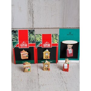 May include: Three miniature Hallmark Keepsake ornaments. The ornaments are in their original boxes. The ornaments are a wooden clock, a wooden dresser, and a mouse holding a red book that says "Don't Worry, Be Happy".