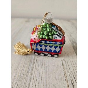 May include: A glass Christmas bauble shaped like a red and blue train carrying a Christmas tree and other gifts. The bauble has a gold tassel.
