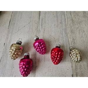 May include: Five vintage glass Christmas ornaments shaped like bunches of grapes. Two are gold, two are pink, and one is red.