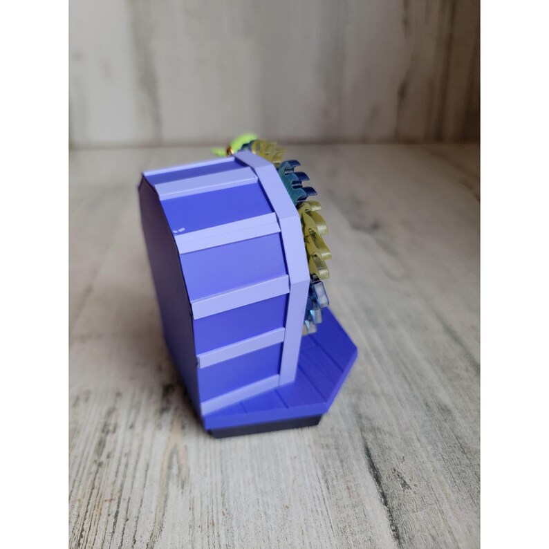 May include: A purple and blue Ferris wheel ornament with a yellow and green top. The ornament is made of plastic and has a detailed design.