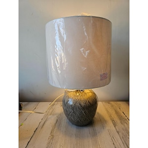 May include: A ceramic table lamp with a white fabric lampshade. The lamp base features a gray and brown patterned design.