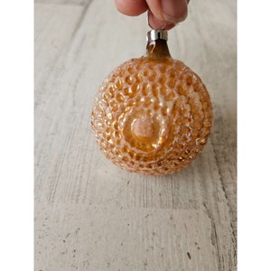 May include: A vintage glass Christmas ornament with a textured, honeycomb-like surface. The ornament is a pale orange color with a white iridescent finish.