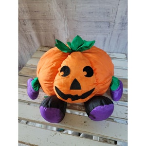 May include: Orange and green plush pumpkin with a black smiling face and purple feet.