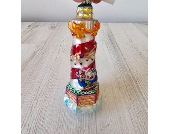 Könnte beinhalten: Dekorative Leuchtturm-Ornament mit rot-weiß gestreiftem Design, goldenen Akzenten und einem blauen Schlitten mit Geschenken. Der Leuchtturm ist etwa 15 cm hoch.