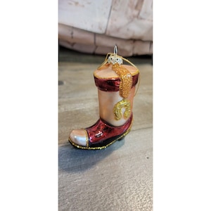 May include: A glass Christmas bauble shaped like a red and gold cowboy boot with a gold horseshoe on the side.