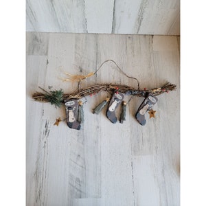 May include: A rustic twig garland with four felt stocking ornaments. The stockings are decorated with snowman faces and have a brown and white color scheme.