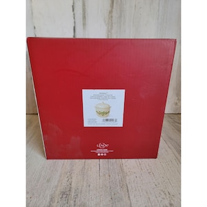 Puede incluir: Una caja roja con una etiqueta blanca que muestra un cuenco color crema con un diseño floral verde y dorado. La caja tiene la palabra "Holiday" impresa en la etiqueta, junto con la marca "Lenox".