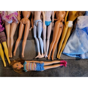 May include: A group of eight dolls with different colored dresses and hairstyles. The dolls are arranged in a row, with their legs spread out. One doll is lying down with pink shoes.