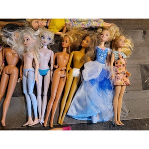May include: A collection of dolls with various hairstyles and outfits. The dolls are wearing dresses, skirts, and pants. Some dolls have long hair, while others have short hair. The dolls are all different colors and have different facial features.