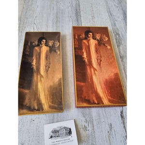 May include: Two framed prints featuring a portrait of a woman in a long, flowing gown. The prints have a gold frame and are set against a warm, sepia-toned background. A small booklet with the White House Historical Association logo is visible.