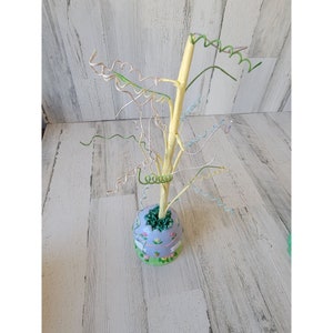 Op de afbeelding: Een pastelblauwe keramische paaseitjesboom met een gele houten stam en kleurrijke gekrulde draadtakken.