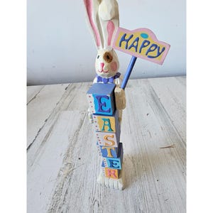 May include: A white wooden bunny rabbit holding a sign that says "Happy" and a stack of colorful blocks that spell out "Easter".