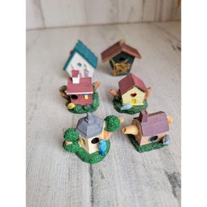 Könnte beinhalten: Ein Set mit sieben Miniatur-Vogelhäusern, jedes mit einem einzigartigen Design und Farbschema. Die Vogelhäuser sind aus Keramik gefertigt und weisen Details wie kleine Fenster, Türen und Vogelsilhouetten auf.