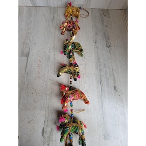 May include: A string of five decorative elephant ornaments. Each elephant is crafted with colorful fabric, gold accents, and beaded details. The elephants are suspended vertically, creating a unique and eye-catching display. The ornaments are suitable for home decor.