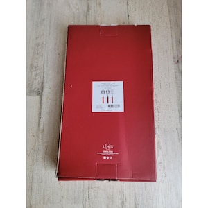 Può includere: Una scatola rettangolare rossa con un'etichetta bianca con illustrazioni di posate. La scatola ha il marchio "Lenox" stampato sopra. La scatola è su una superficie di legno chiaro.