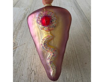 Peut inclure: Ornement de Noël décoratif en forme de goutte d'eau. L'ornement a une finition irisée rose et or. Un bijou rouge est au centre d'un motif floral, avec une tige perlée colorée et incurvée.