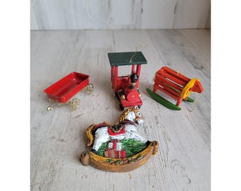 May include: A selection of miniature Christmas decorations. Features a red wagon with gold wheels, a red and green train, a red rocking horse, and a rocking horse ornament with a white horse and a brown base.