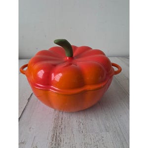 May include: A vibrant, orange and red ceramic pumpkin-shaped casserole dish with a green stem. The dish has two side handles and a matching lid. This decorative kitchenware is ideal for serving and cooking.