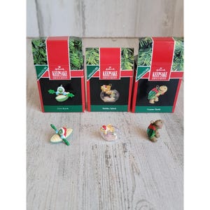 May include: Three miniature Hallmark Keepsake ornaments in their original boxes. The ornaments are a green turtle in a kayak, a goldfish in a bowl, and a green turtle. The boxes are red with white lettering and a green tree design.