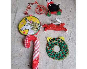 May include: A selection of Christmas decorations. The image shows a red tricycle, a black cat on a red cart, a unicorn, a red and white candy cane, a red spotted rabbit, and a green wreath with red berries.