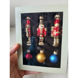 May include: Set of six Christmas ornaments featuring three red and gold nutcracker ornaments and three round ornaments in red, gold, and blue.