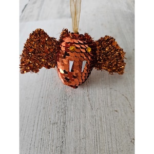 Op de afbeelding: Oranje en gouden pailletten vleermuis ornament met witte tanden.
