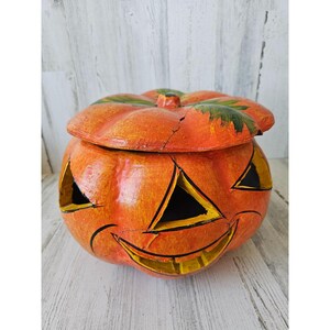 May include: A vintage Halloween pumpkin-shaped candy container with a lid. The pumpkin is orange with a black and yellow painted jack-o'-lantern face. The lid is also orange with green painted leaves.