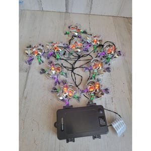 May include: A string of 10 silver skull lights with orange and purple LED lights. The lights are connected to a black battery pack with the words "Made in China" printed on it.