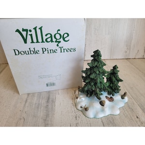 May include: A Department 56 Village Double Pine Trees figurine. The miniature scene features two green pine trees on a snowy base with pine cones. The box is white with green text.