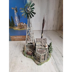 May include: A miniature farm scene featuring a weathered windmill with green blades, a small chicken coop, and a miniature wheelbarrow. The scene includes a small tree and a bundle of dried twigs. The base is a detailed, textured landscape.