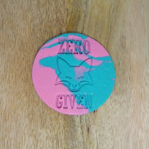 May include: A pink and blue round cookie cutter with the words "ZERO GIVEN" and a fox silhouette.