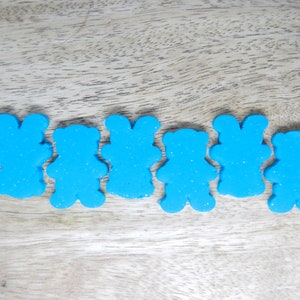 May include: Six blue teddy bear shaped cookie cutters on a wooden surface.