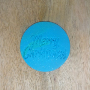 May include: A blue oval-shaped silicone stamp with the words "Merry Christmas" embossed in white.