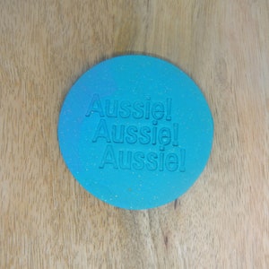 May include: A round, blue cookie cutter with a sparkly finish. The cutter is embossed with the word "Aussie!" repeated three times.
