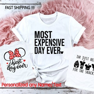 May include: Three white t-shirts with black text and graphics. The first shirt says "Most Expensive Day Ever". The second shirt says "Best Day Ever" and has a red and white Minnie Mouse bow. The third shirt says "I'm Just Here For The Snacks" and has a Mickey Mouse ice cream cone, a Mickey Mouse cup, and a Mickey Mouse lollipop.