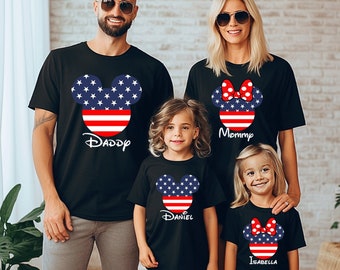 May include: A family of four wearing black t-shirts with American flag Mickey Mouse and Minnie Mouse designs. The shirts say "Daddy", "Mommy", "Daniel", and "Isabella".