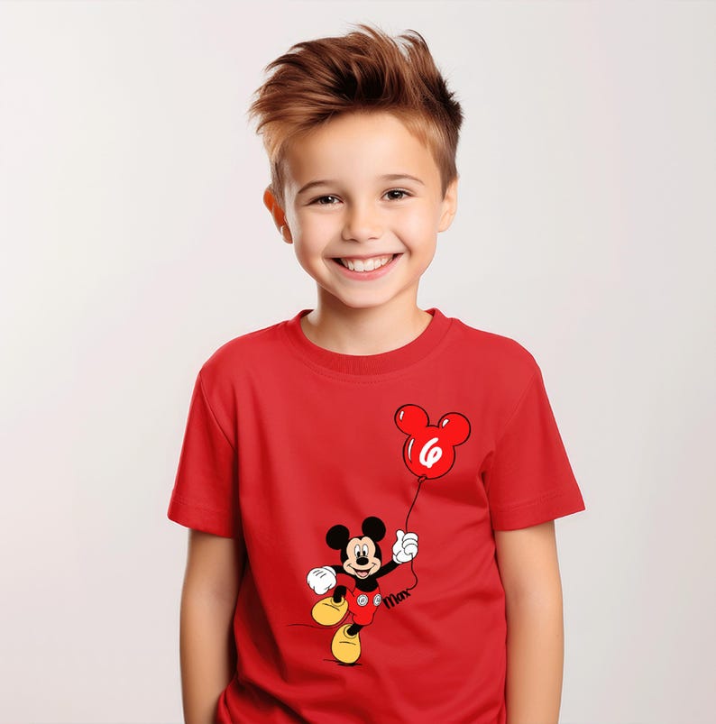 May include: A red t-shirt with a Mickey Mouse cartoon design holding a red balloon with the number 6. The short-sleeved shirt is worn by a smiling child.